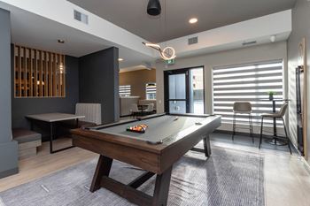 A pool table is in the middle of a room with a chair and a bar stool.