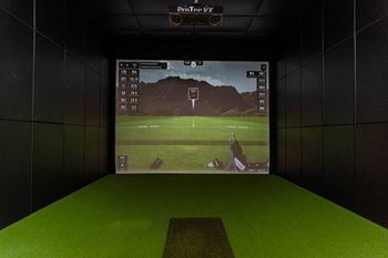 A golf simulator setup with a screen showing a golfer on a course.