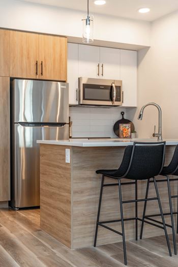 A kitchen with a stainless steel refrigerator, a microwave above the counter, and two black barstools.