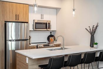 A modern kitchen with a white countertop and black chairs.
