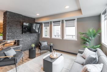 A living room with a grey couch, a black chair, a black coffee table, a stone fireplace, and a flat screen tv mounted on the wall.