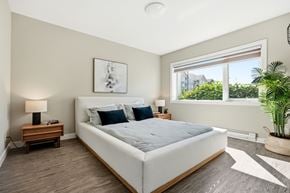 Winnipeg apartment for rent - A bedroom with a large bed, a nightstand with a lamp, and a window with a view of the outside.