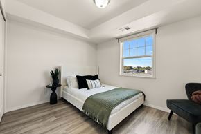 Regina apartment for rent - A bedroom with a bed, a chair, and a window with a view of the sky.