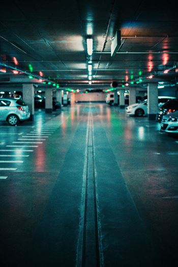A parking garage with cars parked on both sides and a few cars driving through.