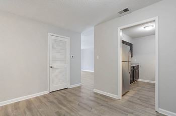 A room with a white door and a kitchen area in the background.