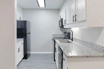 A kitchen with a black fridge, white cabinets, and granite countertops.