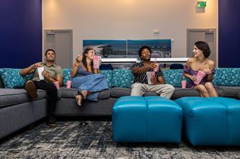 Three people are sitting on a couch eating popcorn and watching a movie.