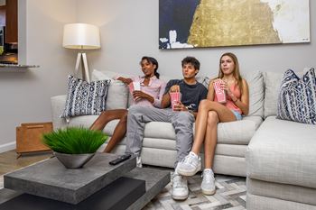 Three people are sitting on a couch with popcorn and watching television