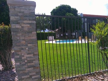 Sierra Vista apartment for rent - A black metal fence surrounds a grassy area with a pool in the background.