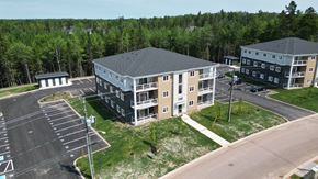 Dieppe apartment for rent - A parking lot in front of a building with a grassy area and trees in the background.