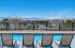 Denver apartment for rent - A pool surrounded by chairs and a fence with a mountain range in the background.
