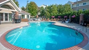 Rochester apartment for rent - a large pool with chairs and a building in the background