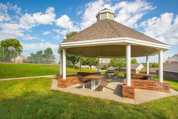 A gazebo with a brick base and a brown roof is surrounded by a grassy area.