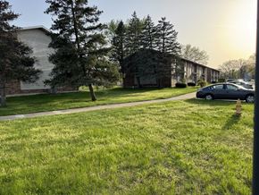 Elkhart apartment for rent - A grassy area in front of a building with a tree and a car parked on the side.