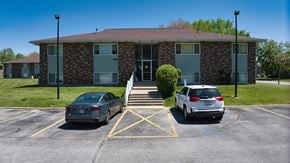 Goshen apartment for rent - Two cars are parked in a parking lot in front of a brick building.