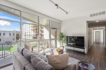 A modern living room with a grey sofa and a large window overlooking a cityscape.