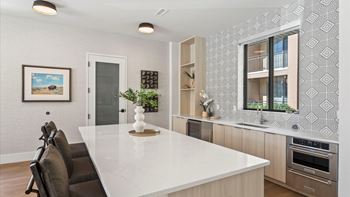 A modern kitchen with a white countertop and brown chairs.