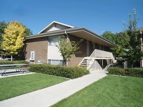 Orem apartment for rent - A building with a brown roof and a white awning is surrounded by greenery.