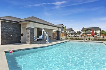 A swimming pool in front of a house with a person sitting on a chair.
