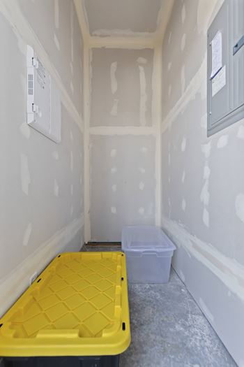 A yellow plastic container sits on a grey floor in a room with white walls.