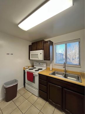 Orem apartment for rent - A kitchen with a white microwave, a white oven, a brown trash can, brown cabinets, a brown countertop, and a brown sink.