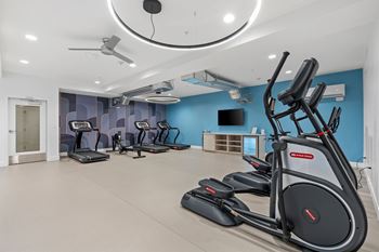 A gym with a row of treadmills and elliptical machines.