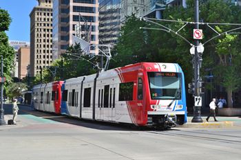 A red and white train is on the tracks in a city.
