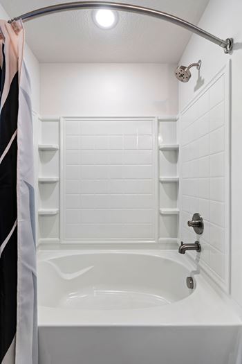 White bathtub with tiled walls and recessed shelving