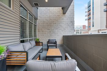 A patio with a grey couch, wooden table and a black chair.