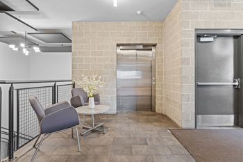 A grey chair is in front of a brick wall.