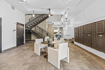 A spacious room with a staircase, a table with chairs, and a wall of mailboxes.