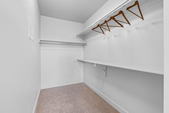 A white closet with a carpeted floor and a white shelf.