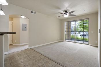 A spacious living room with a ceiling fan and sliding glass doors leading to a balcony.