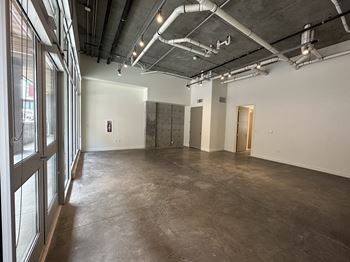 A large empty room with a concrete floor and walls, and a ceiling with exposed pipes and ducts.