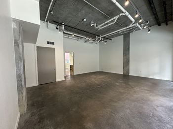 A large empty room with concrete floors and walls, and a ceiling with exposed pipes.