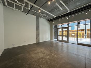 A large, empty room with a concrete floor and a view of a construction site through the windows.