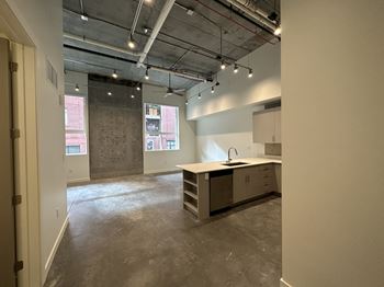 A large, empty room with a kitchenette and a window overlooking a cityscape.