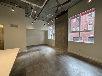 A large empty room with a white table and a window overlooking a red building.