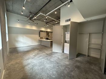 A large, empty room with a kitchenette and a refrigerator.