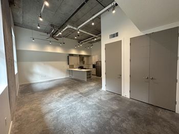 A large, empty room with concrete floors and walls, and a ceiling with exposed pipes and lights.