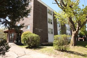 Kingston apartment for rent - A brick building with a sign that says "The Sandpiper 300" is surrounded by trees and bushes.