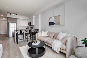 Calgary apartment for rent - A modern living room with a grey couch, a coffee table, and a dining area in the background.