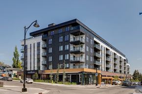 Calgary apartment for rent - A modern multi-story building with a parking lot in front.