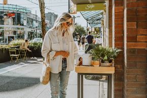 Vancouver apartment for rent - A woman in a white jacket and ripped jeans stands on a sidewalk next to a table with a potted plant on it.
