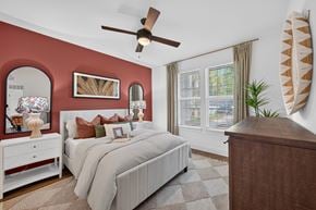 Ponte Vedra apartment for rent - A bedroom with a large bed, a dresser, and a ceiling fan, the wall behind the bed is painted a soft red with a mirror above the bedside table