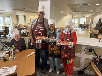 Four people in christmas aprons and hats holding pizzas