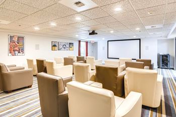 A conference room with a white screen and beige chairs.