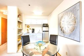 King City apartment for rent - A dining room with a glass table and chairs, a framed artwork on the wall, and a kitchen area in the background. at King City Senior Village Apartments, King City, 97224