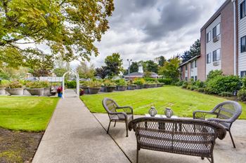 A patio with a bench and chairs is surrounded by a grassy area and apartment buildings.