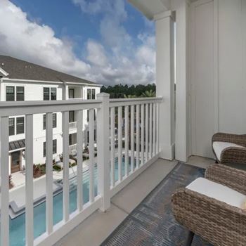 A white balcony with a pool and chairs.